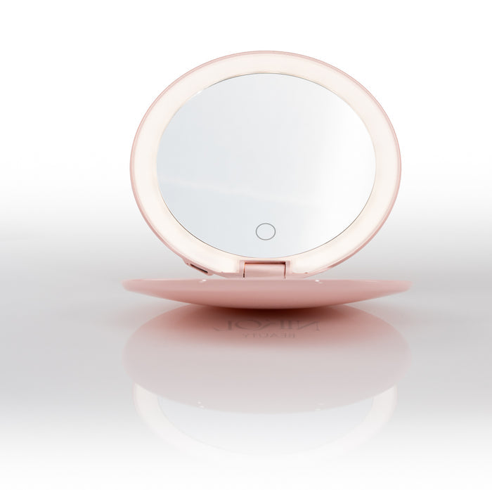 The Nikol Beauty 10x Magnification Mirror, a round pink rechargeable makeup mirror with a built-in LED ring light, shown open and standing upright cordless on a reflective white surface.