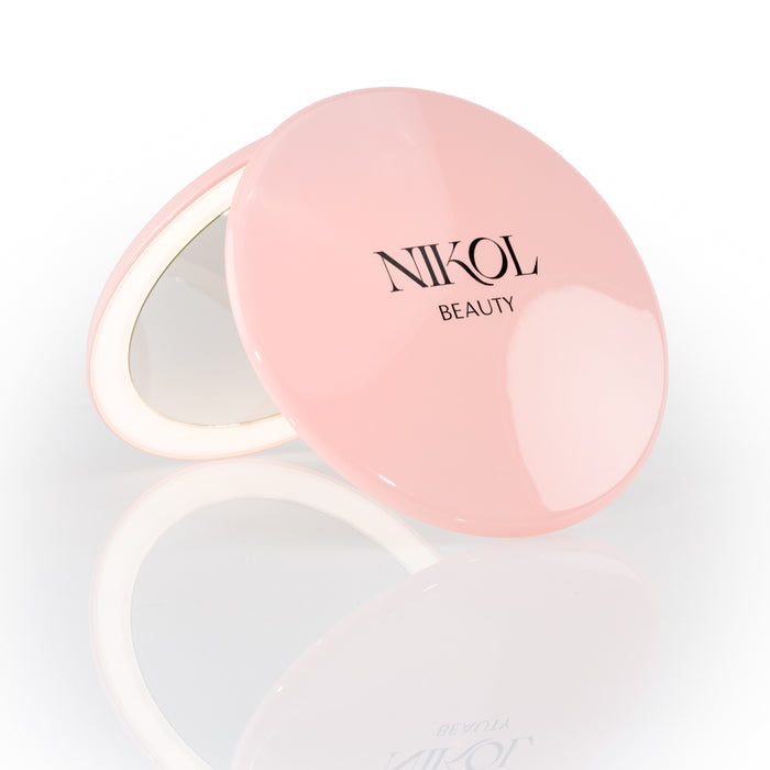 The Nikol Beauty 10x Magnification Mirror is a round, pink compact with the brand name on the lid, partially open to display its precise mirror, shown against a white background—perfect for detailed makeup touch-ups.
