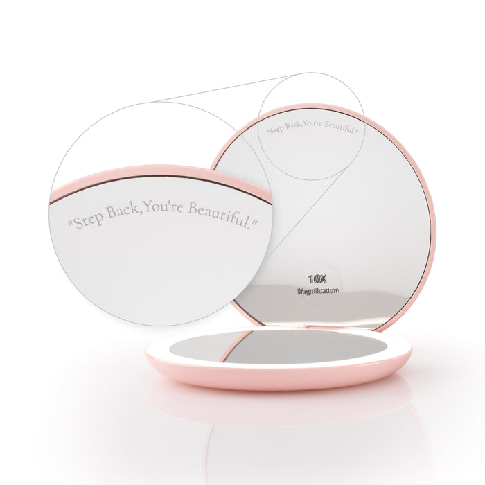 The Nikol Beauty 10x Magnification Mirror is round with a pink frame and features an engraved "Step Back, You’re Beautiful" phrase plus a "10X Magnification" label on the reflection.