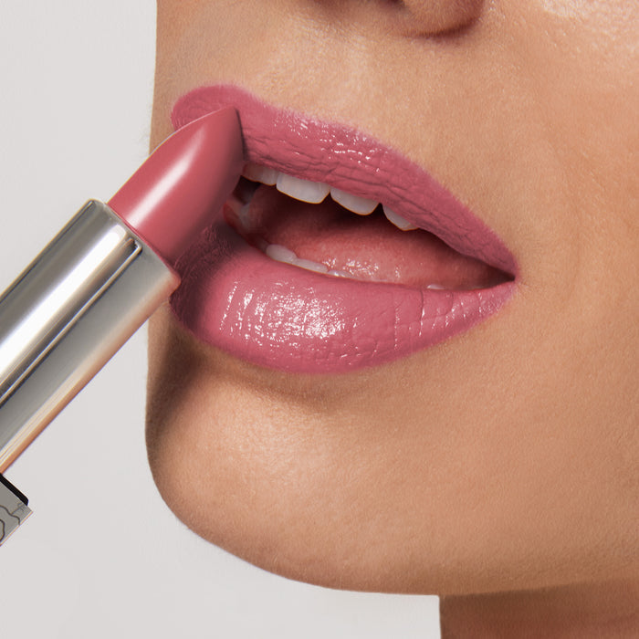 A person applies Nikol Beautys Actually, I Can Shiny Velvet Cream Lipstick #33. The ultra-creamy pink hue highlights the parted lips, showcasing the glossy, hydrating texture against a neutral background.