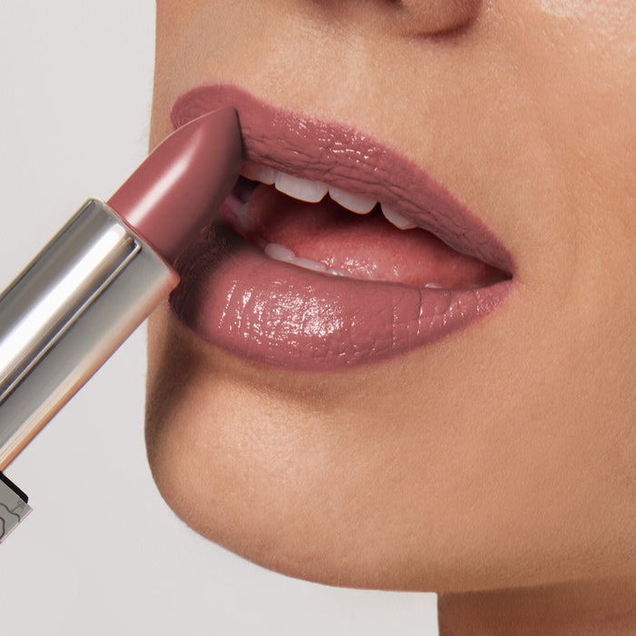 Close-up of someone applying Nikol Beautys Aperitif Shiny Velvet Cream Lipstick #419, highlighting its smooth, glossy finish and hydrating, cruelty-free formula; a perfect match for mature lips against a soft, neutral background.