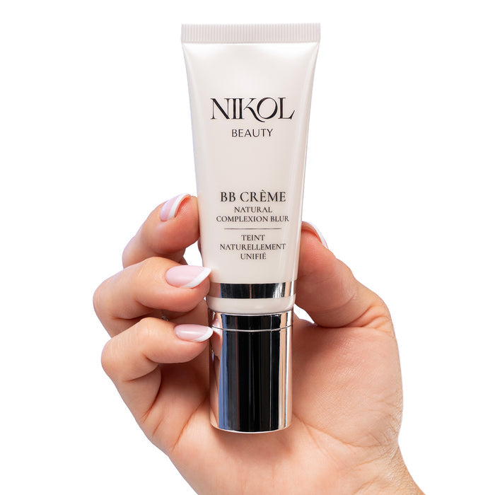 A hand with manicured nails holds a tube of Nikol Beauty BB CRÈME, enriched with Vitamin C, against a white background—perfect for enhancing the radiance of mature skin.