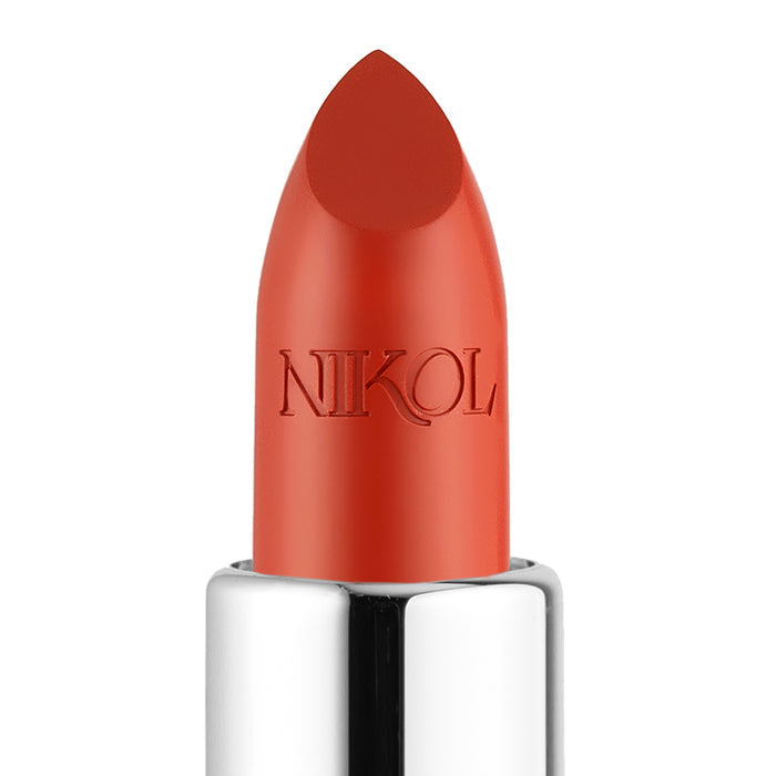 Close-up of Beach House Shiny Velvet Cream Lipstick #122 from Nikol Beauty, in a vibrant orange-red shade. This hydrating lipstick, enriched with shea butter for smooth application and nourishment, features a shiny silver base contrasting with the plain white background and has the brand name engraved on the bullet.