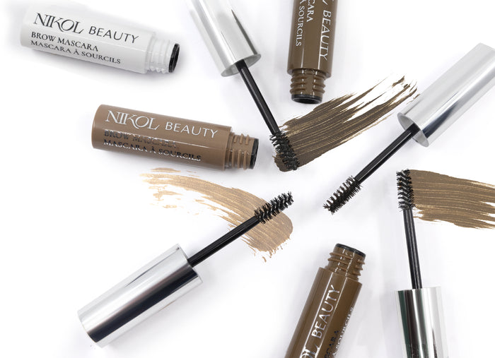 Open tubes of Nikol Beautys Brow Mascara in different shades are displayed with brushes and swatches on a white background. Nearby, the open caps highlight the high-pigment colors designed for beautifully defined eyebrows.