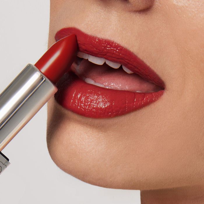 Close-up of someone applying Nikol Beautys Confidence Shiny Velvet Cream Lipstick #173, a bright red with an ultra-creamy, hydrating formula. Only slightly parted, the mature lips reveal its rich color and glossy finish as the lipstick bullet angles toward the upper lip.