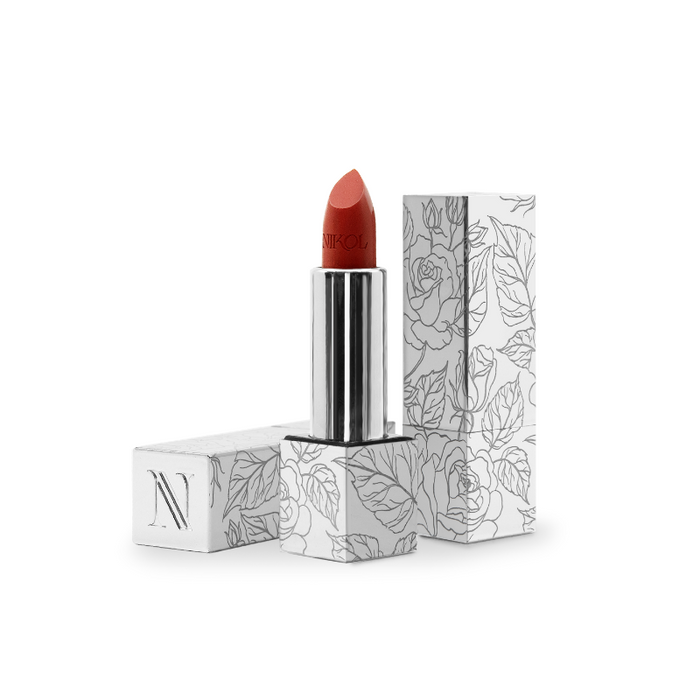 The Confidence Shiny Velvet Cream Lipstick #173 by Nikol Beauty, with its ultra-creamy texture, stands upright, partially uncapped. The cap beside it showcases a floral pattern and an N, highlighting its hydrating effect on mature lips.