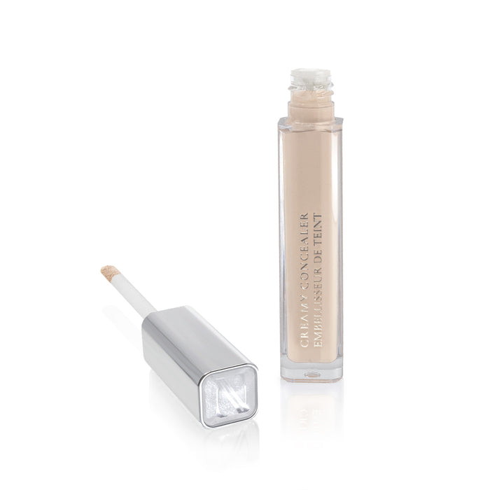 A tube of Nikol Beautys Creamy Concealer, featuring a square silver cap, reveals an applicator wand when removed. This high-coverage light beige concealer is perfect for makeup application and stands elegantly on a reflective white surface, accentuating its sleek design.
