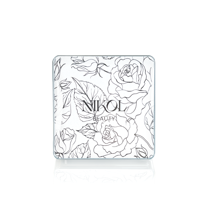 The Crème Brûlée compact by Nikol Beauty features an intricate black and white floral pattern with roses and leaves on the lid. Inside, it offers a cruelty-free bronzer ideal for adding a sun-kissed glow to mature skin.