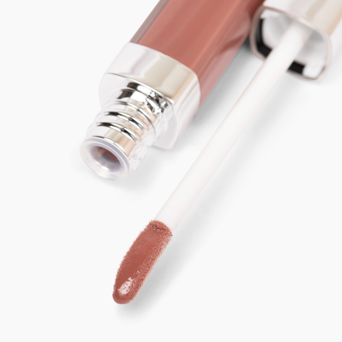 An open tube of Nikol Beautys Good Vibes Lip Gloss #443 showcases a high-impact shine with a shiny silver cap and white wand. The rosy pink gloss promises comfortable wear, with the partially blurred tube resting on a white surface.