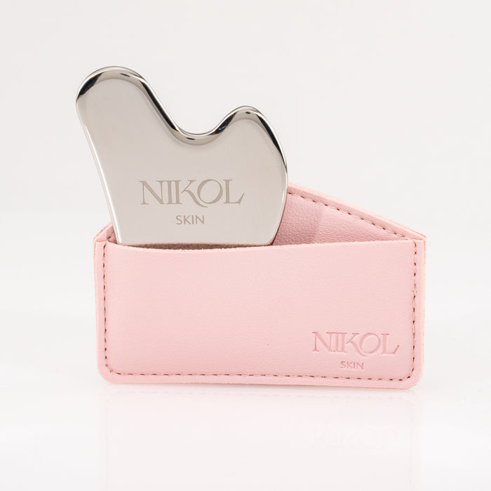 A silver Gua Sha Stainless Steel facial massage tool by Nikol Beauty, partially placed in a light pink leather holder embossed with the brand name, ideal for lymphatic drainage, set against a white background.