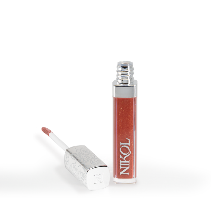 A tube of Ignite Lip Gloss #176 by Nikol Beauty stands upright with its silver, floral-engraved cap and applicator beside it on a white background—ideal for the mature woman seeking a brilliant copper shimmer.