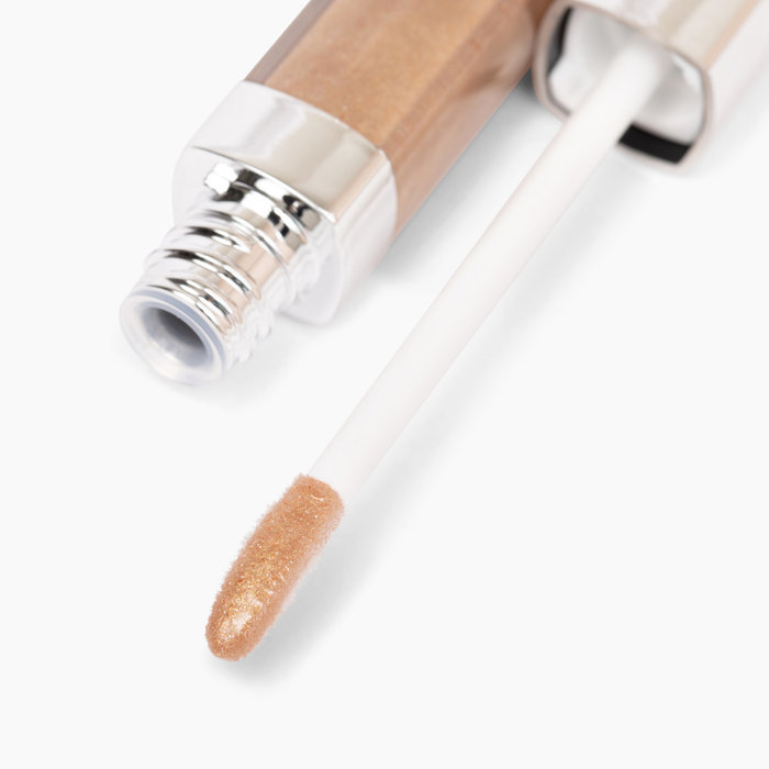 A close-up of Nikol Beautys Manifest & Glow #183 lip gloss tube reveals its gold glitter finish and nourishing avocado oil benefits. The applicator wand is partially out, showing the shiny metallic product tip. Sleek packaging boasts a reflective cap.