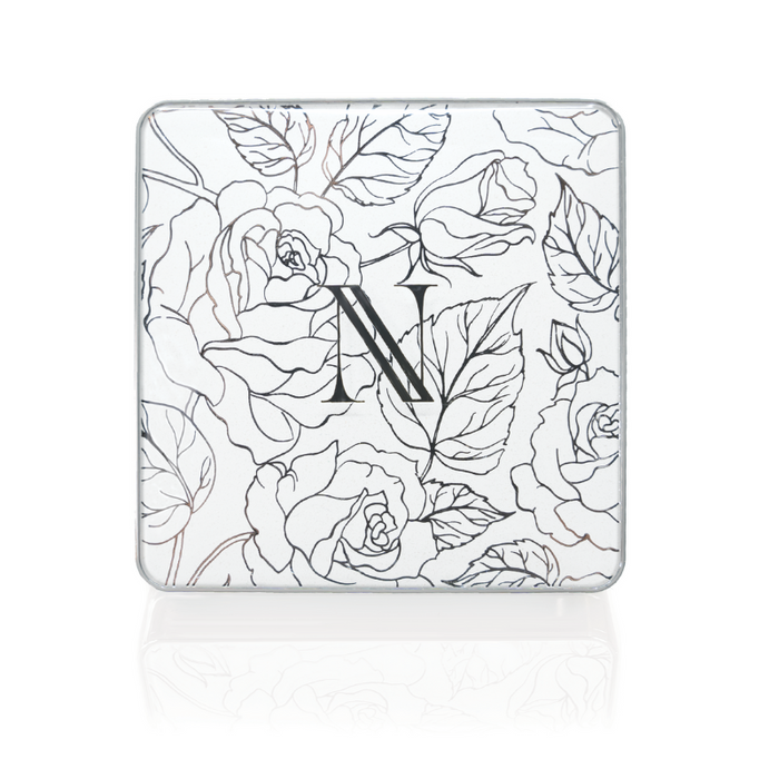 Square tin with a floral design of roses and leaves on a white background, featuring the letter N from Nikol Beauty in the center, adding elegance. Its part of the Naughty Nancy 3-Well Eyeshadow Palette.