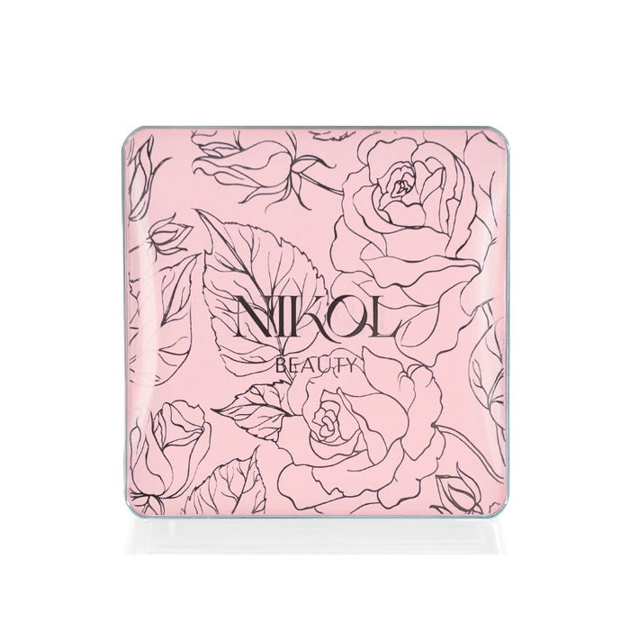 A light pink square compact with black floral rose and leaf designs features Nikol Beauty at the center. The Nikita Banana Brightening Powder delivers a flawless finish with its pressed powder formula.