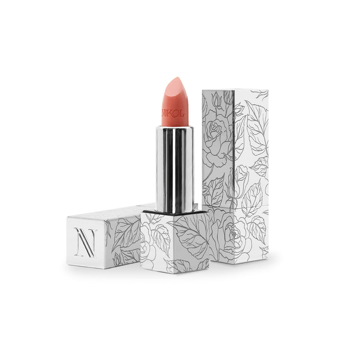 The NikRay Shiny Velvet Cream Lipstick #701 by Nikol Beauty, perfect for mature lips, stands upright in its sleek silver casing. The box, mostly white with black floral line art, complements the peach-colored hydrating lipstick, highlighting its cruelty-free formulation.