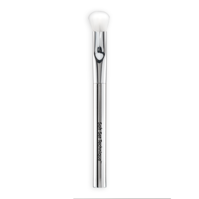 The Nikol Beauty SOFT SET TECHNIQUE™ BRUSH is a silver vegan makeup brush with a white, soft bristle head and "Softer Than Couture" on the handle, perfect for under-eye setting and shown on a white background.