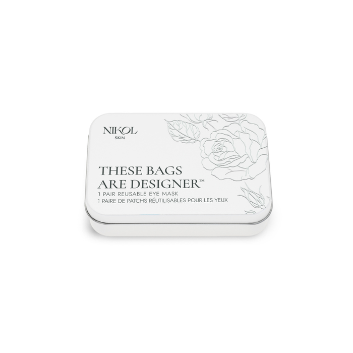 A rectangular white tin labeled "These Bags Are Designer-Eye Mask" by Nikol Beauty contains a reusable, medical-grade silicone eye mask with a floral design and bilingual English/French text.